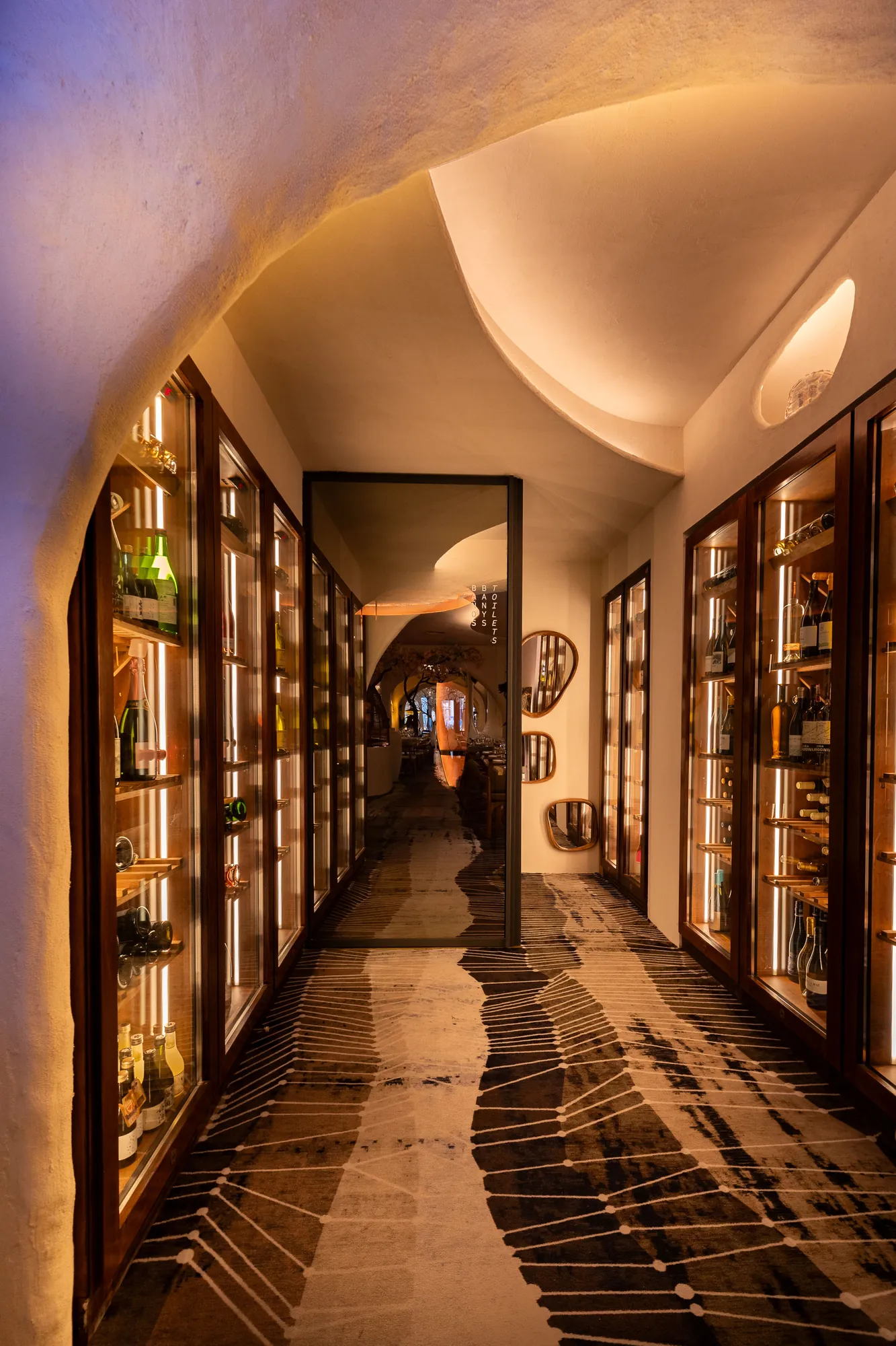 Pasillo de vinotecas iluminadas bajo una bóveda blanca